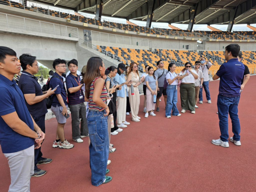 Near the wide entrance of the Athletic Stadium in New Clark City, students of PA 152 MWV gather
closely around a BCDA officer. The officer gestures while speaking, providing historical background and
explaining the stadium’s design elements. The students listen attentively, some holding water bottles or phones for taking notes, absorbing insights about one of the country’s key sporting infrastructures.